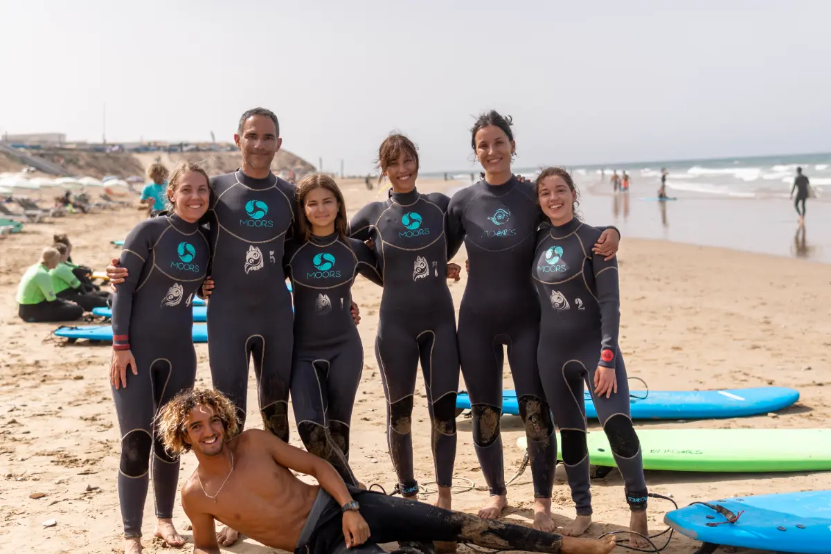 A happy family in wetsuits pose with surfboards on a sunny beach in Morocco, ready for or just finished a surf lesson. This image represents the fun experience at a surfcamp in Taghazout or Tamraght.