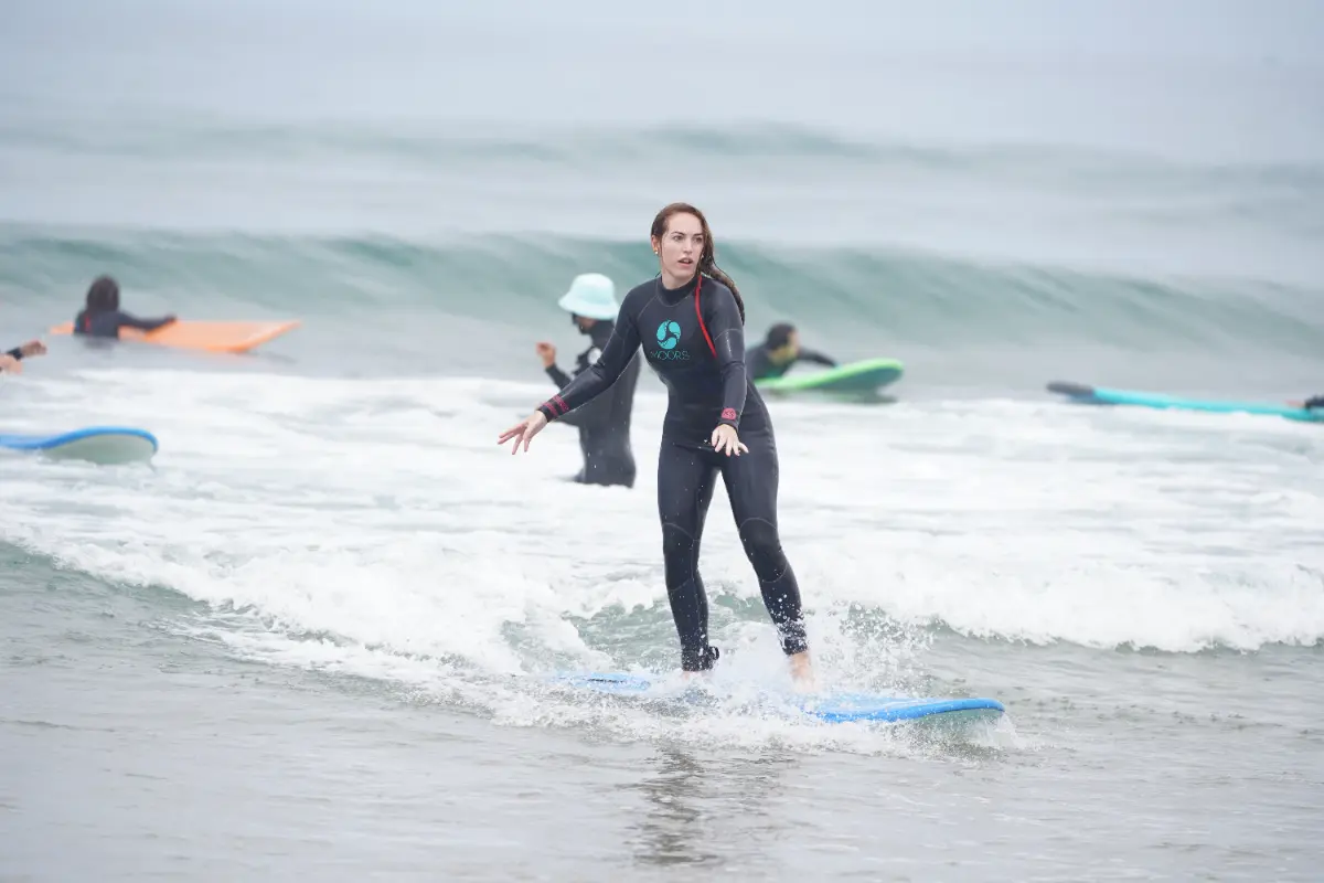 Young woman riding a blue surfboard during a surf lesson, a typical scene at a surfcamp in Morocco like Taghazout or Tamraght. Features a beginner surfboard and the experience of riding a small wave.