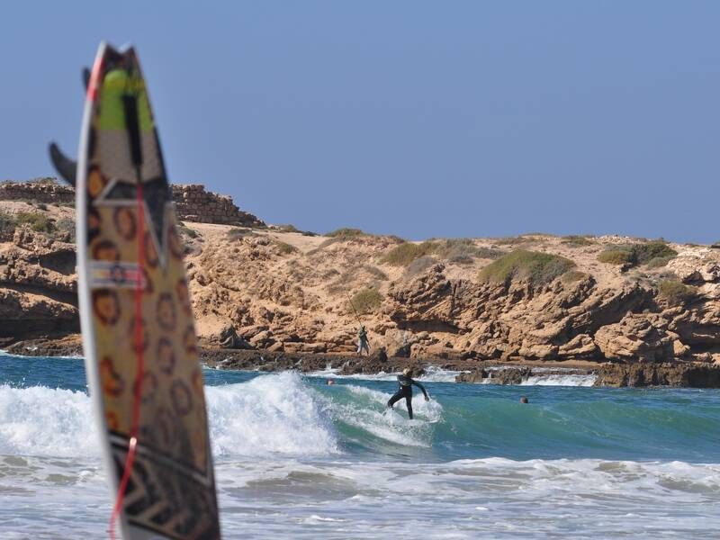 Surfer riding a wave at Devil's Rock beach in Tamraght with a surfboard in the foreground