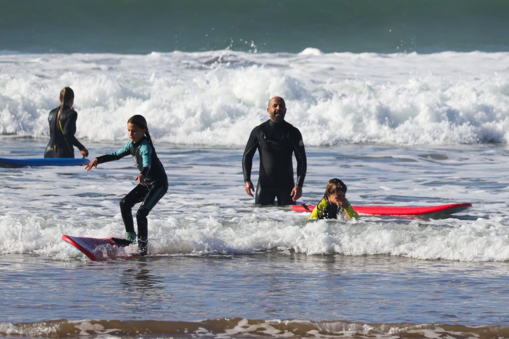 Ung pige står op på sit surfboard under surfundervisning for børn i Marokko