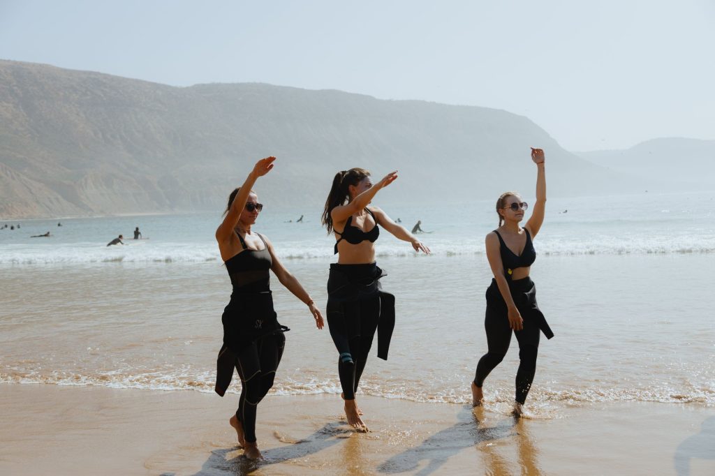 Three friends in wetsuits dancing on the beach in Imsouane after surfing