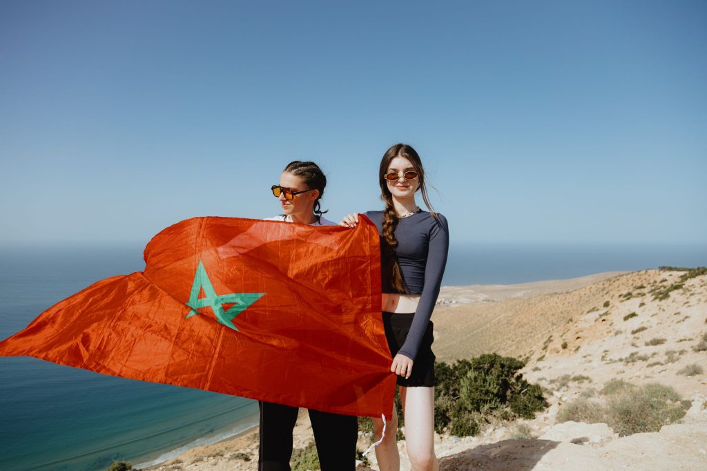 Two travellers holding a Moroccan flag on the hill above Imsouane bay