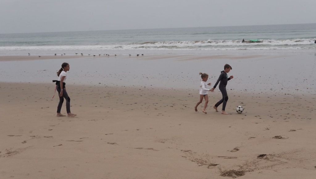Børn spiller fodbold på stranden på surfferie med familien i Marokko