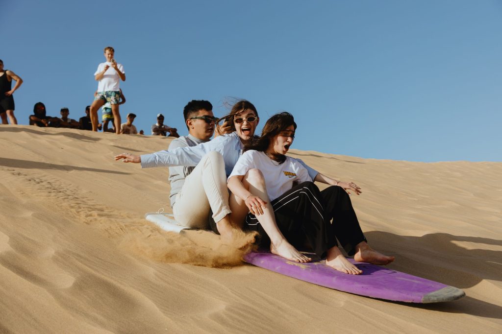 Två vänner som glider ner för sanddynerna i Timlaline tillsammans på en sandboard
