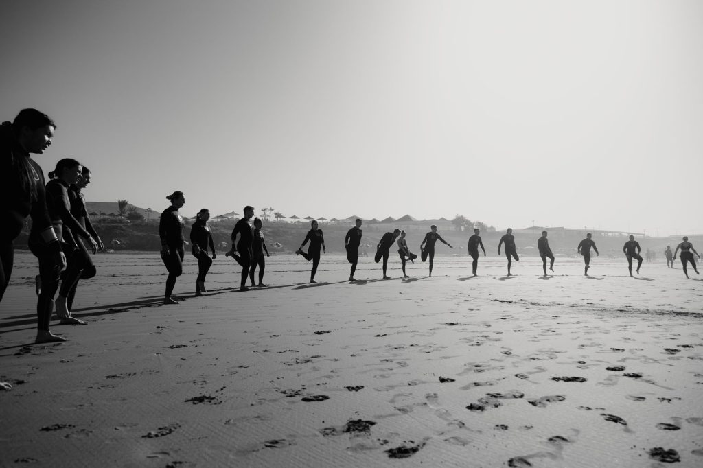 Foto en blanco y negro de una clase de surf calentando en la playa de Crocro, Tamraght